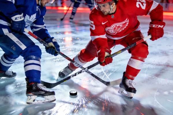 NHL比赛中，红翼队球员在防守时与对手争抢冰球的激烈场面